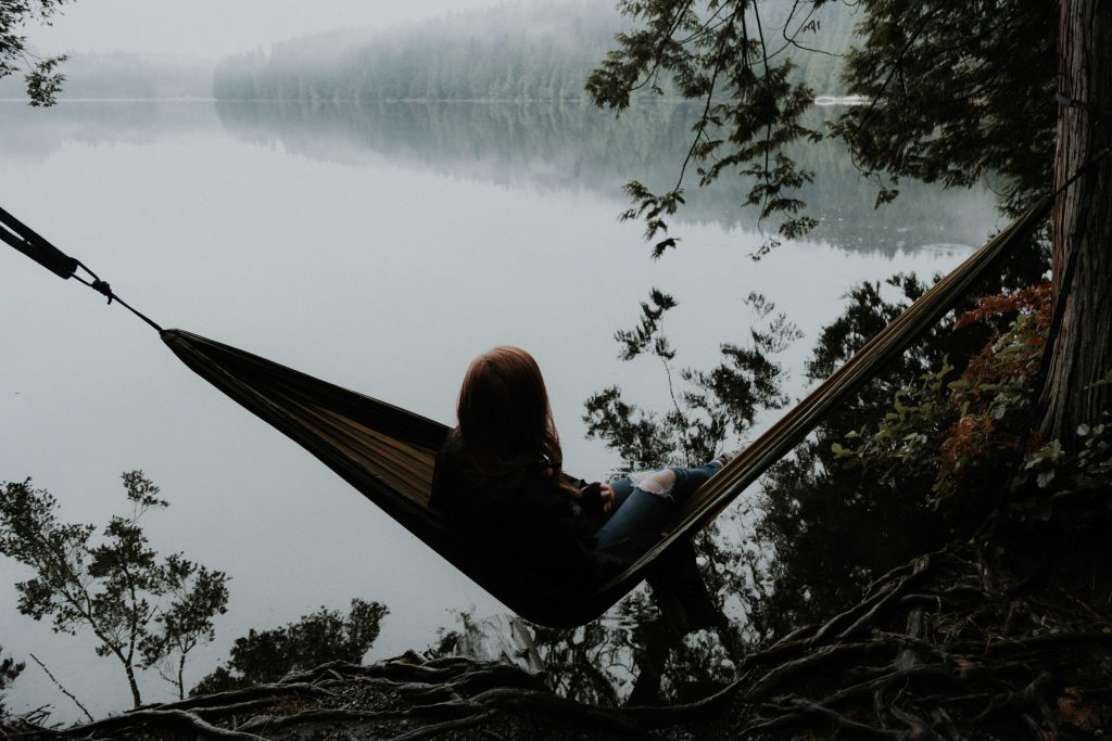 Woman sitting on a hammock facing a lake